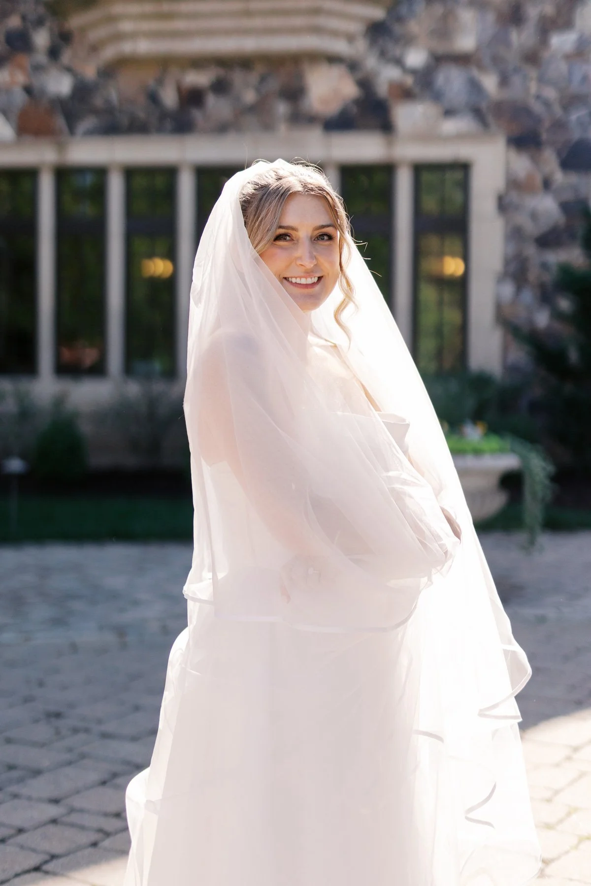 Bride in full veil smiling confidently in natural light with soft natural glam makeup