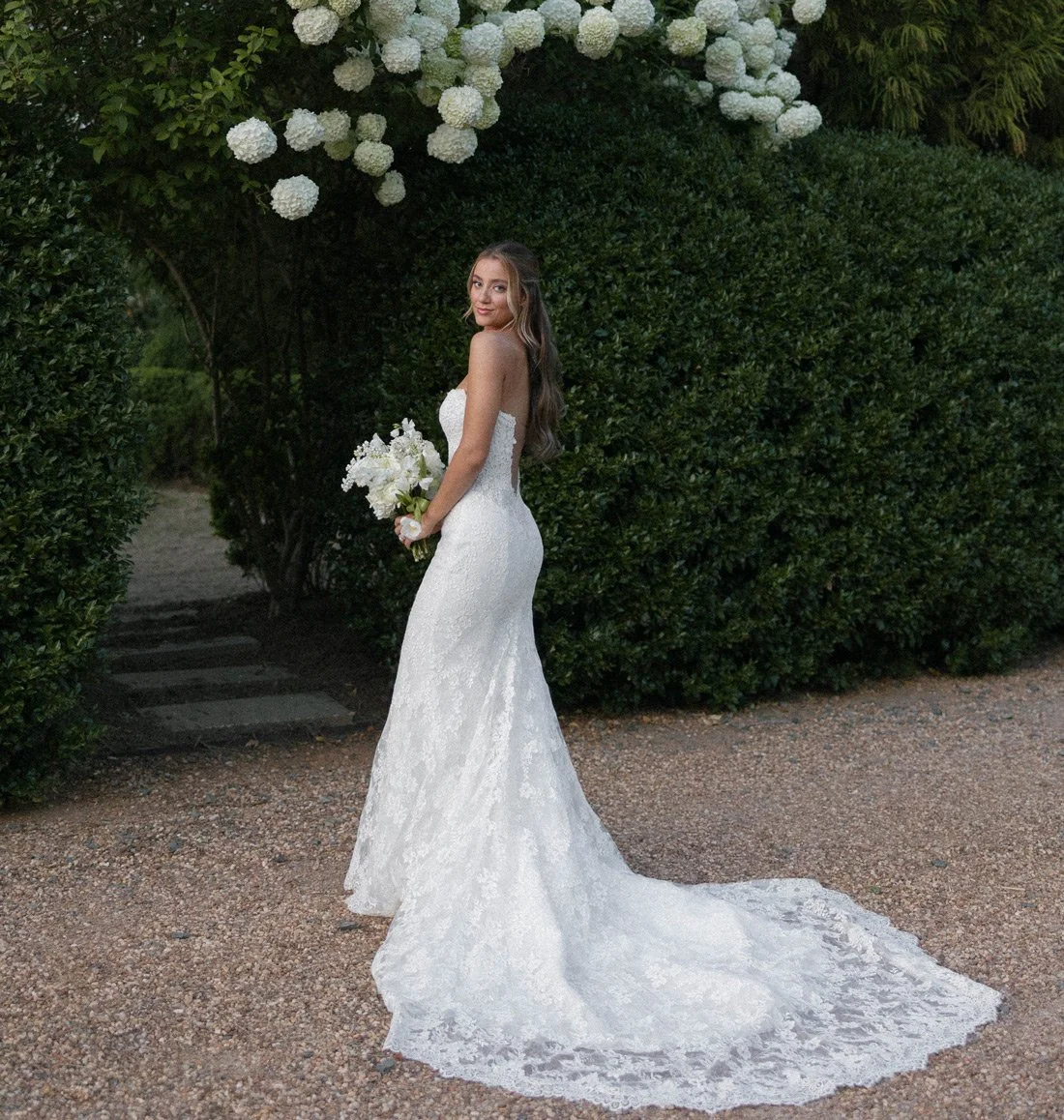 Bride posing outdoors in lace gown with natural makeup and romantic hairstyle in Charlotte