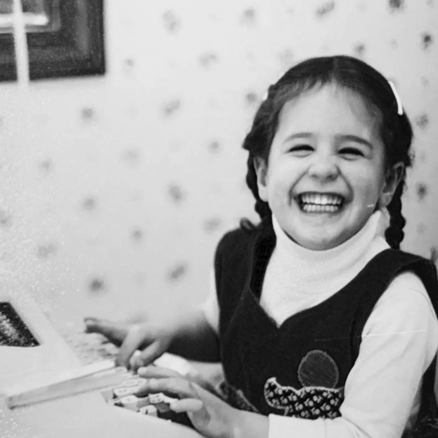 A young girl with braids and a hair clip, smiling and playing a keyboard.