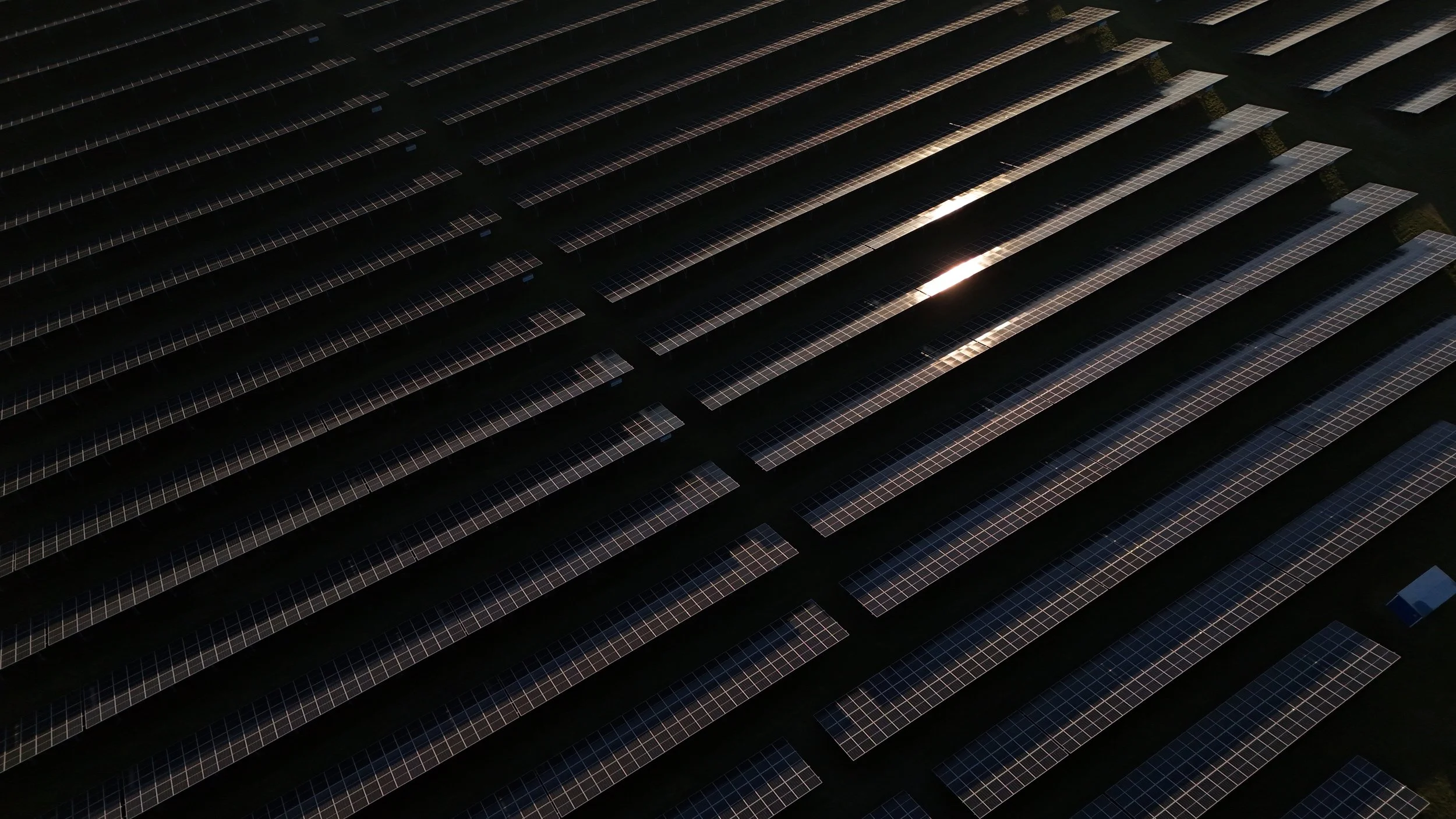 Luftaufnahme eines Solarparks mit mehreren Reihen von Solarpanelen bei Sonnenuntergang.