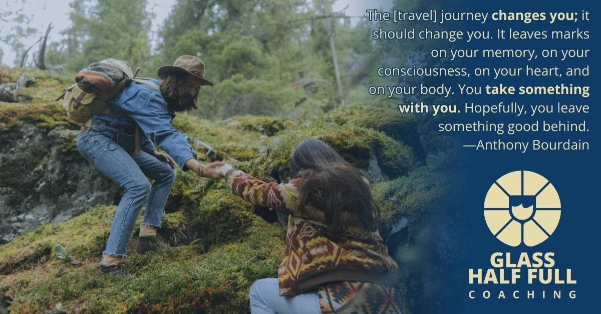 A man in outdoor gear helping a woman climb up a moss-covered, rocky hillside in a forested area. The scene symbolizes support and guidance during a journey.