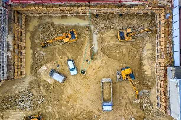 aerial view of a construction site with excavators, a truck, and dirt excavation area surrounded by wooden barriers