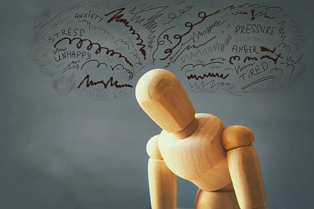 A wooden mannequin with lines and words above its head representing stress, anxiety, frustration, pressure, anger, sadness, unhappiness, and exhaustion.