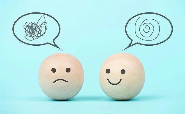 Two wooden balls with simple facial expressions, one sad and the other happy, with speech bubbles above them showing chaotic scribbles and spiral patterns respectively.