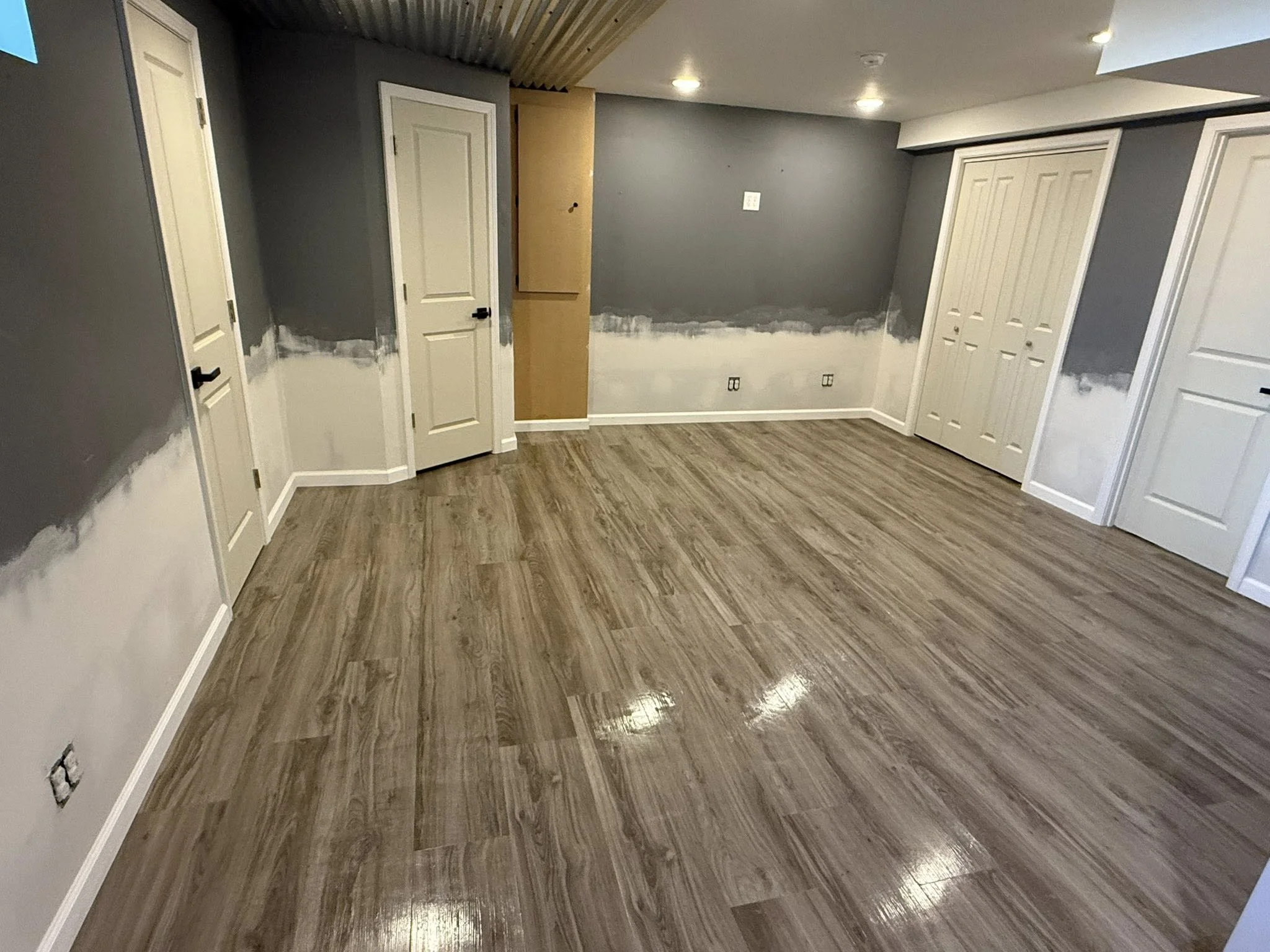 Room undergoing renovation with painted walls and new wood flooring, some walls partially painted gray and white.