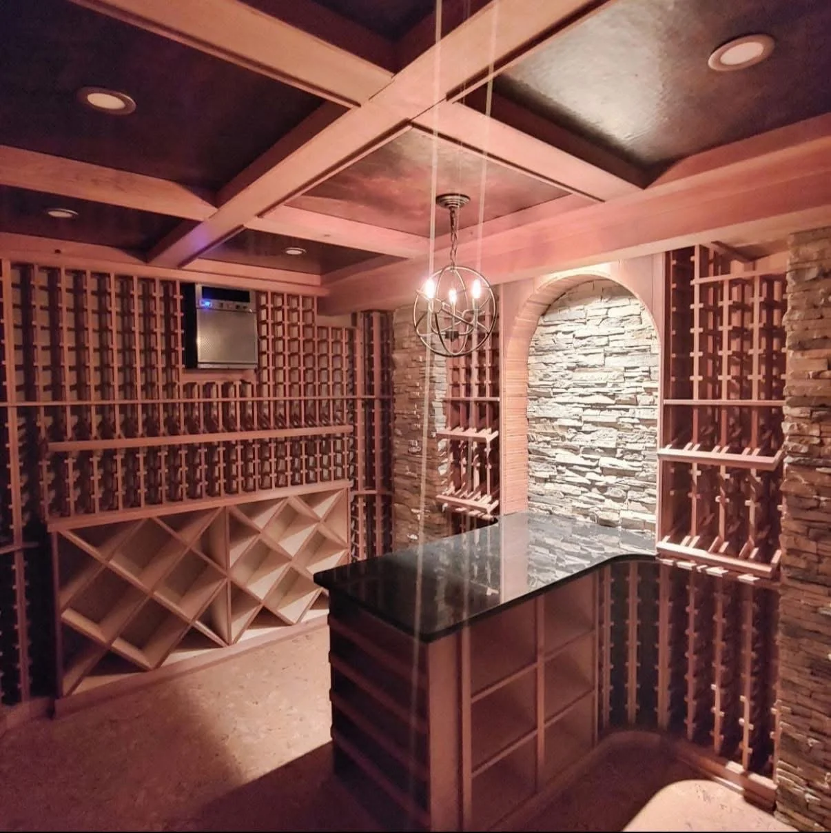 A wine cellar with wooden wine racks, a stone accent wall, a black countertop, and a decorative chandelier.