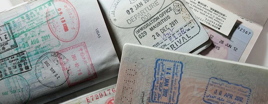 Close-up of multiple stamped and visa pages from passports, featuring various official stamps and cancellations in different languages.