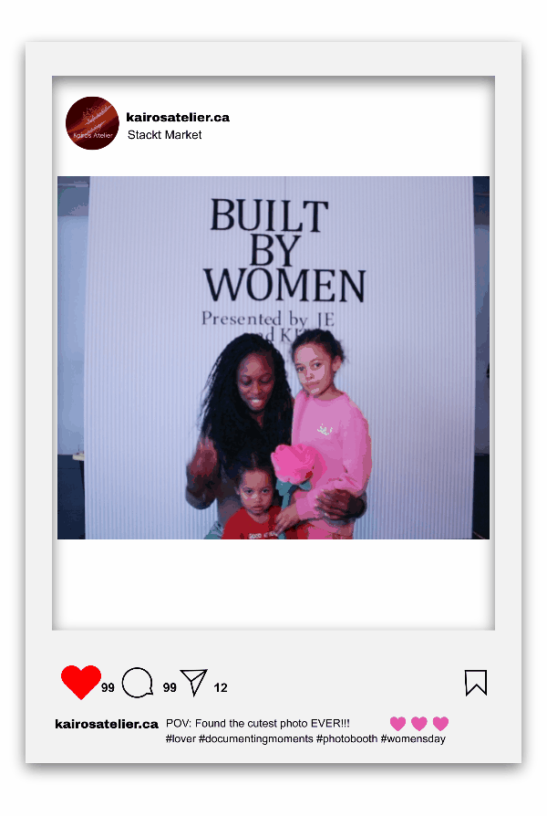Three women and two children posing in front of a sign that reads 'BUILT BY WOMEN' at Stackt Market' s Women's Day Market in Toronto.  one woman is holding a pink stuffed animal, and everyone is smiling.