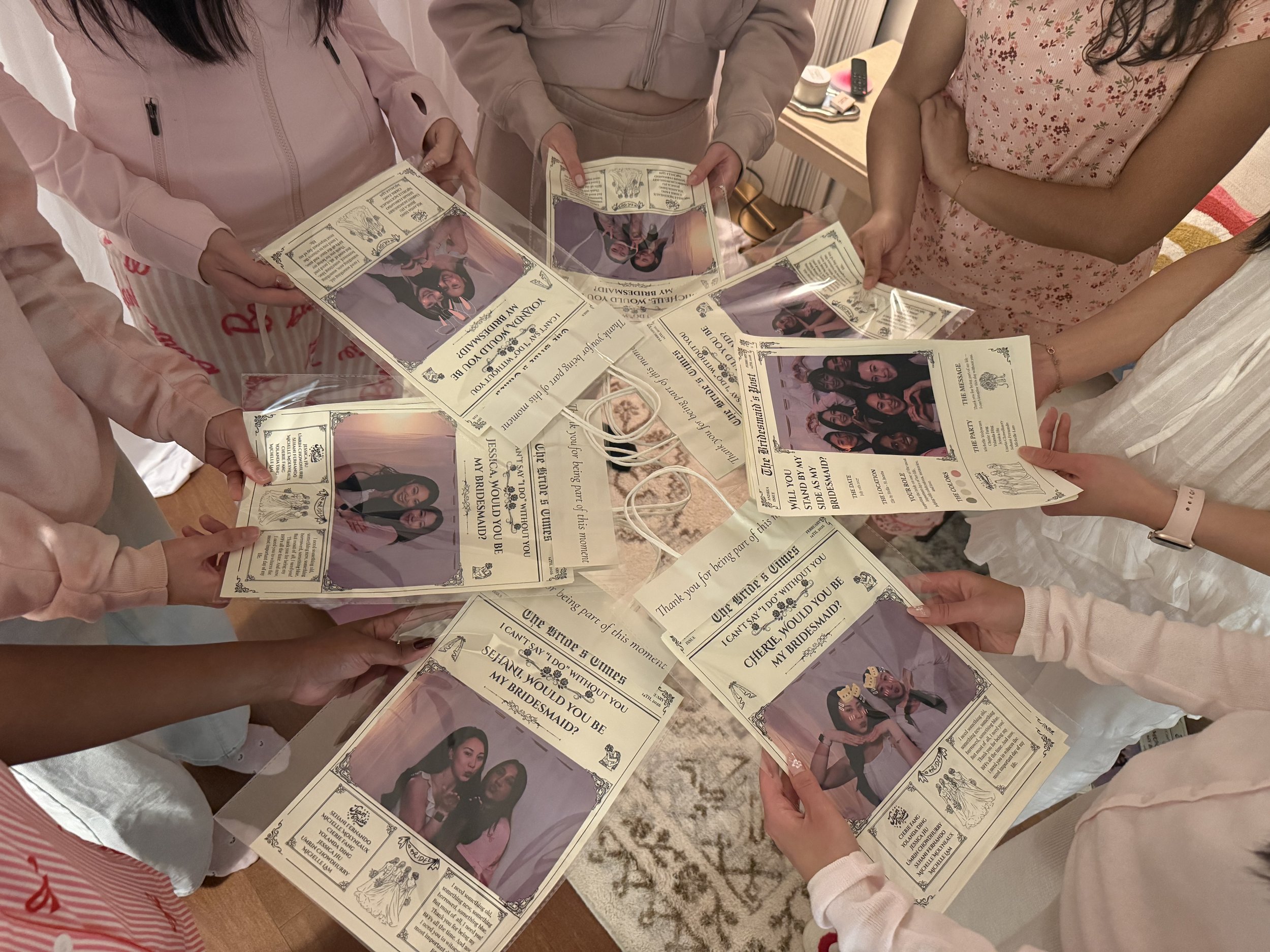 Group of women holding printed bridesmaid proposals resembling vintage tickets with photos and text, gathered around a table.