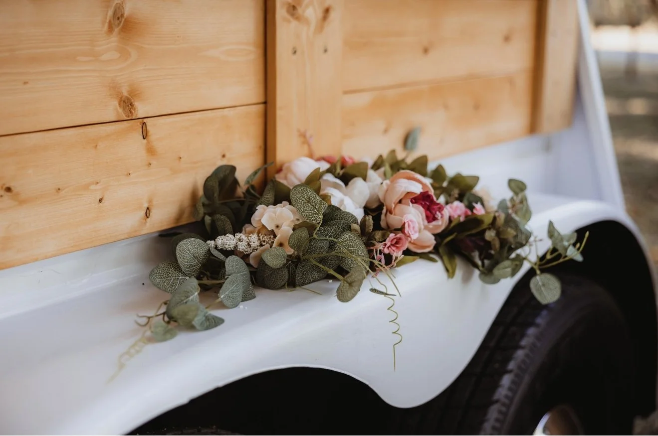 Flowers and greenery arranged on the edge of a white trailer with a wooden siding background.