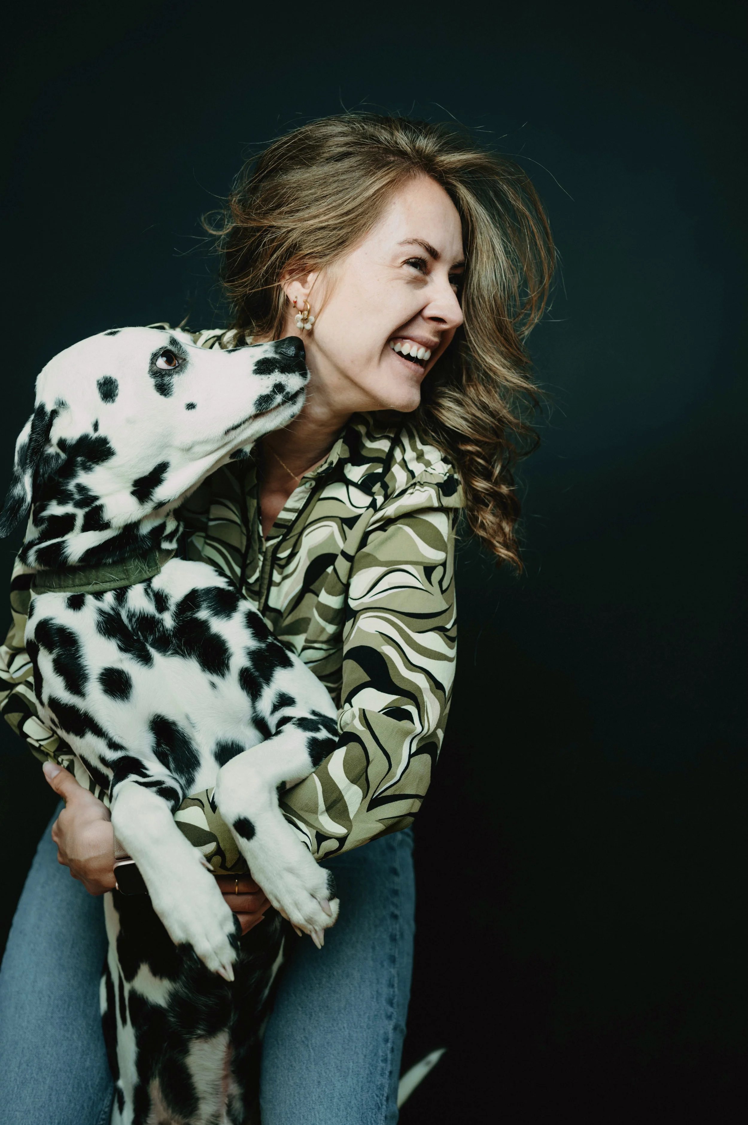 Frau hält Dalmatiner-Hund und lacht, dunkler Hintergrund.