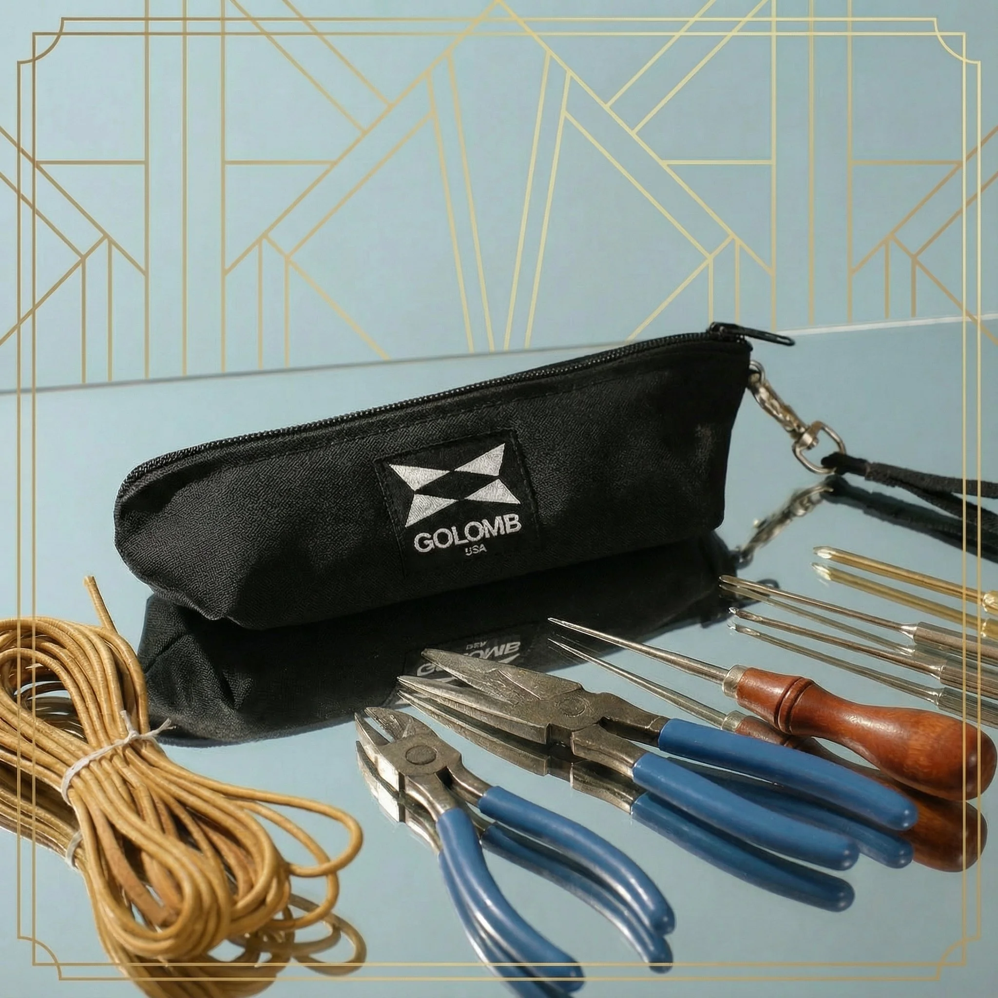 A collection of jewelry-making tools, including pliers, screwdrivers, and a bundle of elastic cords, positioned on a reflective surface with a black pouch labeled "GOLOMB" nearby, and a decorative blue and gold geometric background.
