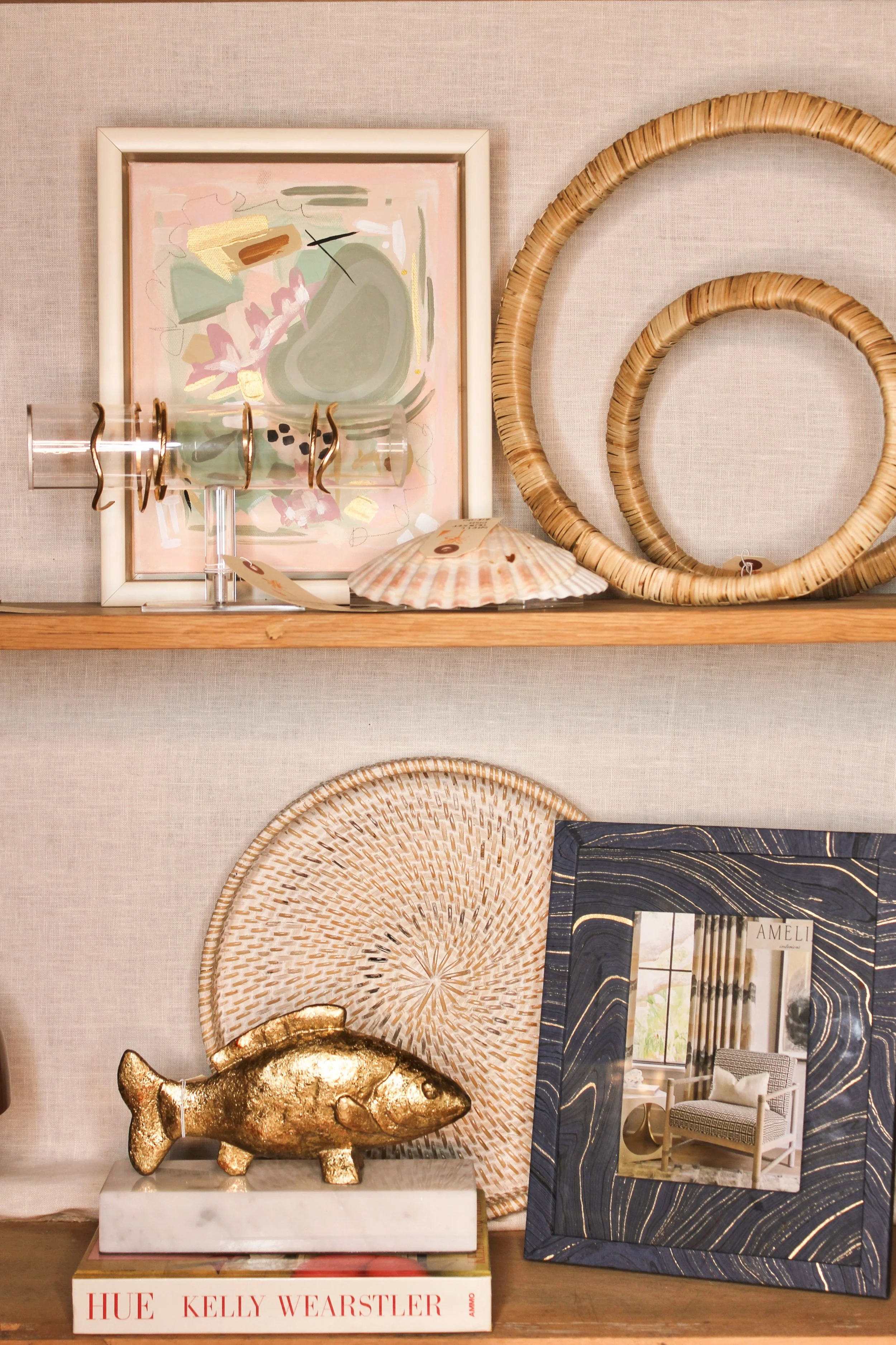Decorative home decor items on two shelves, including framed artwork, wicker hoops, a gold fish sculpture, and a mirror.