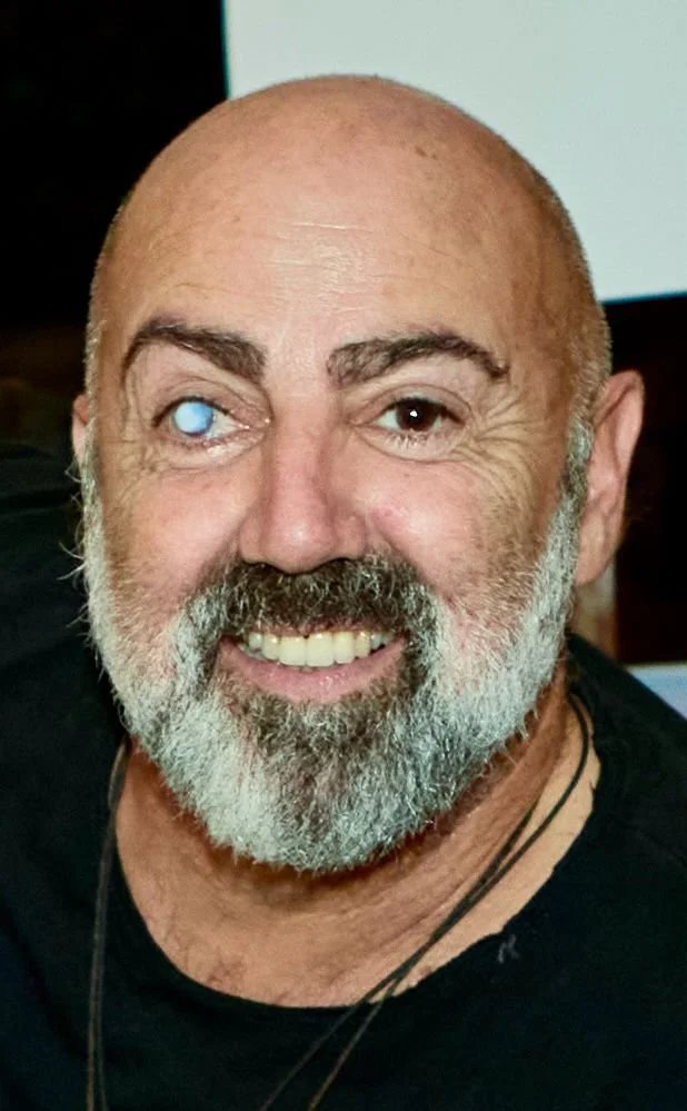 Smiling man with a beard and a cloudy left eye.