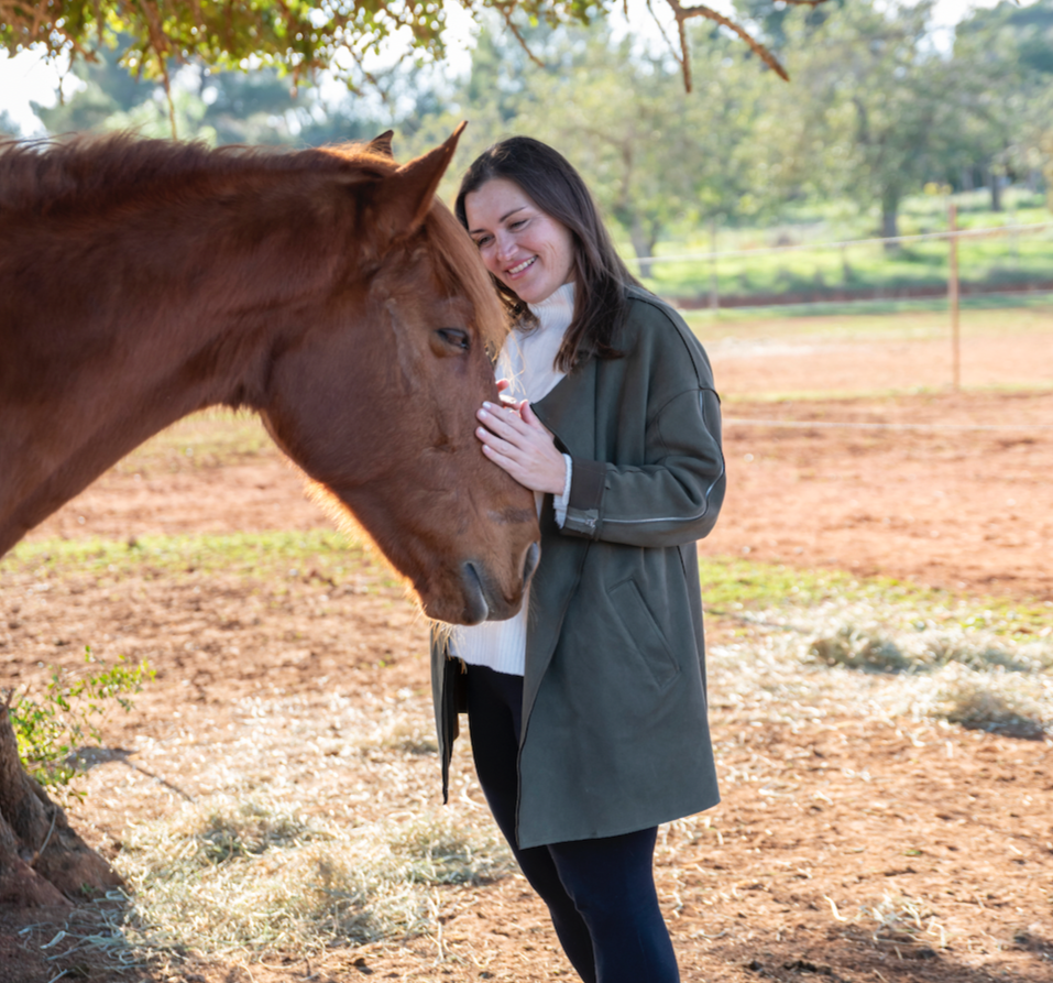 A woman smiling and touching a brown horse on its forehead outside in a fenced area.