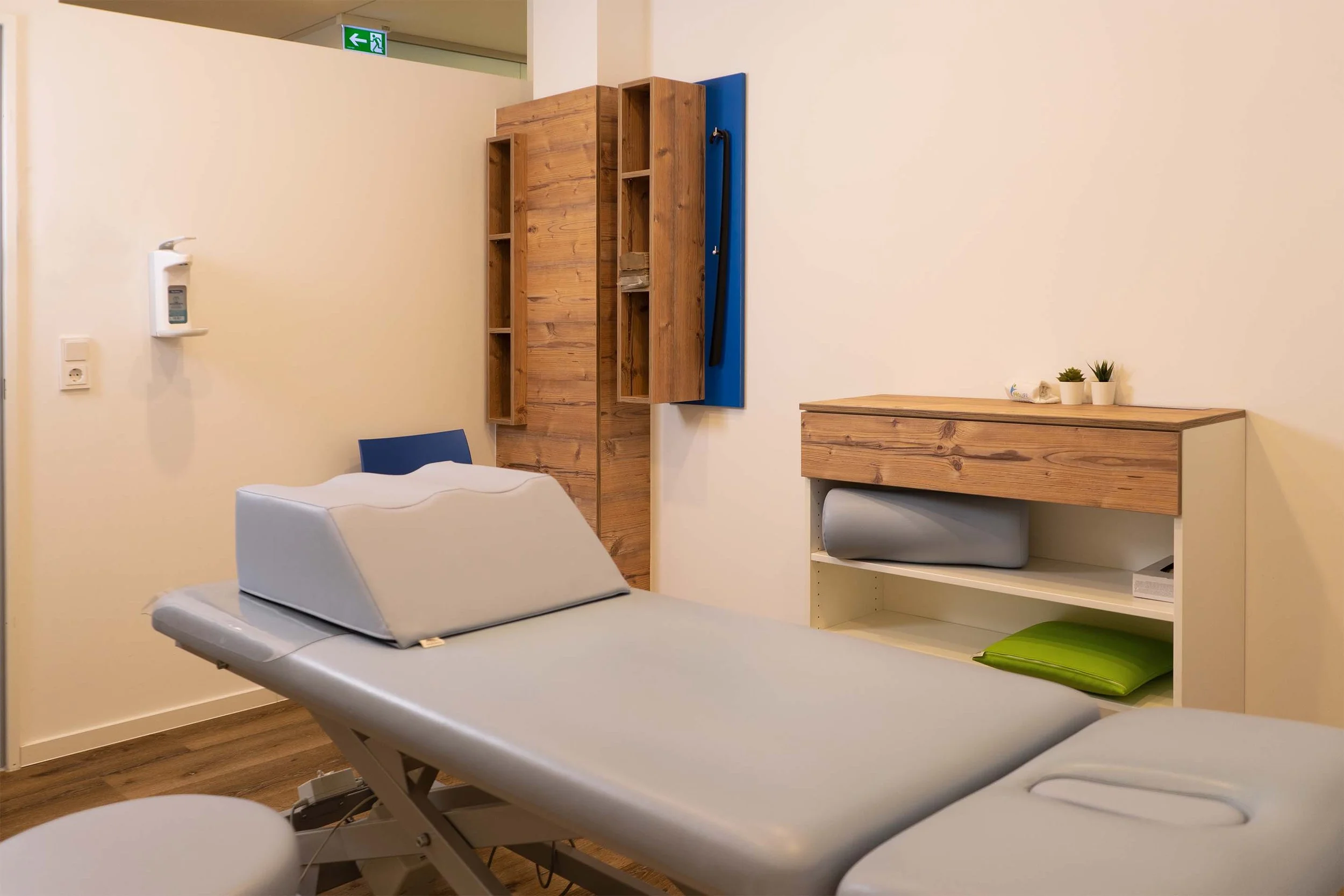 Behandlungsraum mit Liege, Holzregale, Schublade, Pflanzen, Desinfektionsmittelspender.