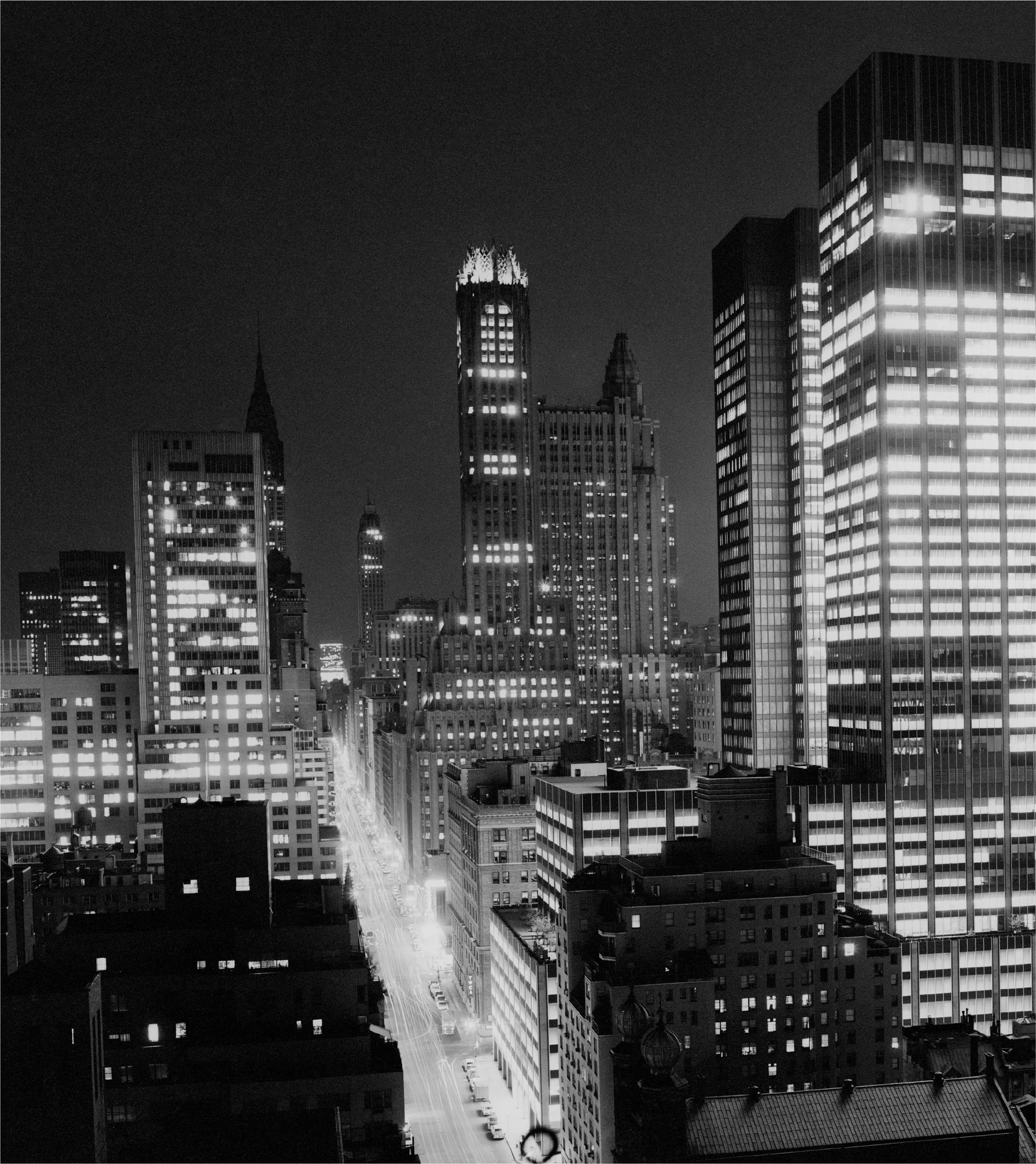 Nighttime cityscape with illuminated skyscrapers and busy streets in a metropolitan area.