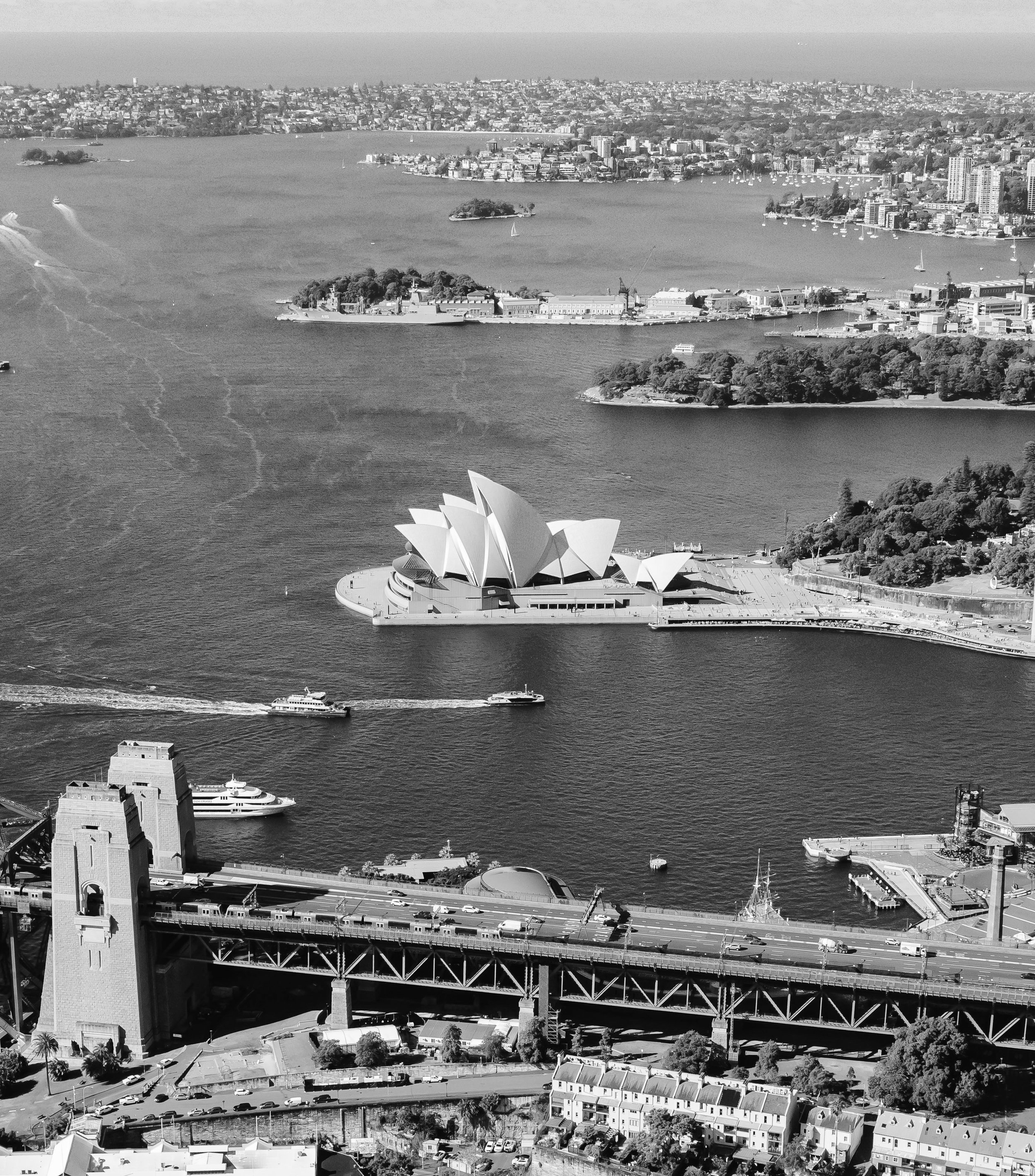 Aerial view of Sydney Harbour with the Sydney Opera House, several boats on the water, and the Harbour Bridge.