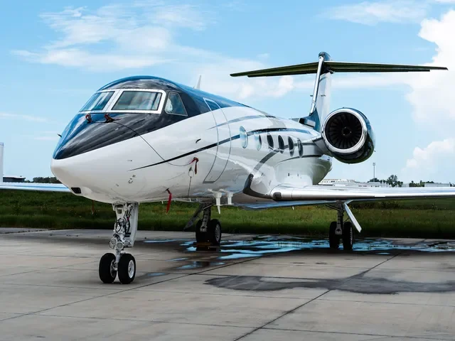 Small private jet parked on an airport tarmac with a blue sky and some clouds in the background.