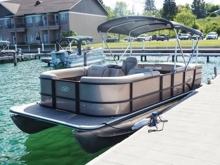 A beige pontoon boat docked at a marina on a sunny day.