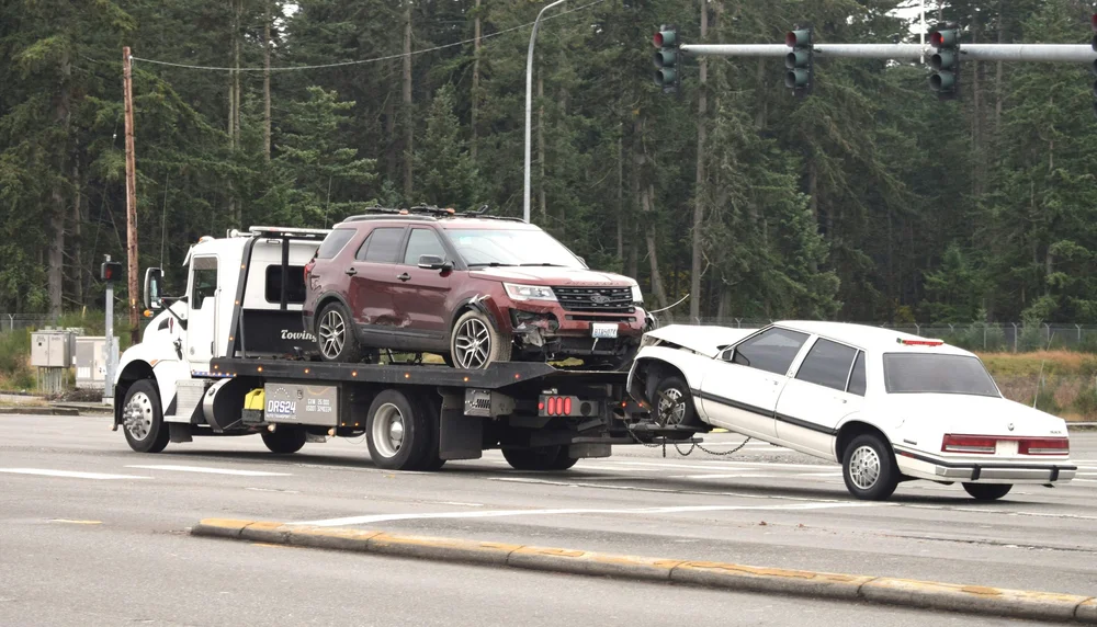 White tow truck hauling two vehicles on a rollback
