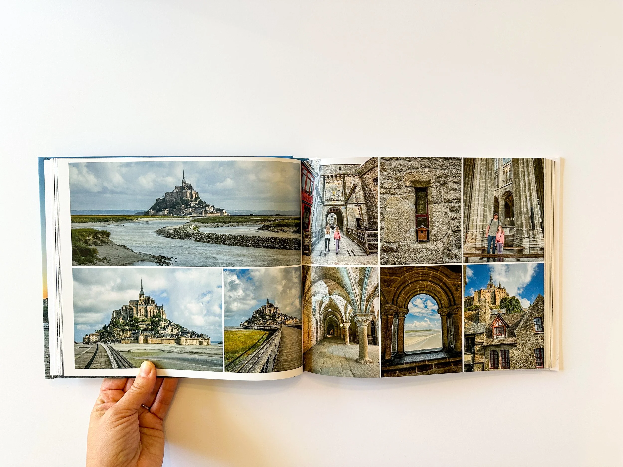 Open travel photo book showing images of Mont Saint-Michel and its interior architecture.