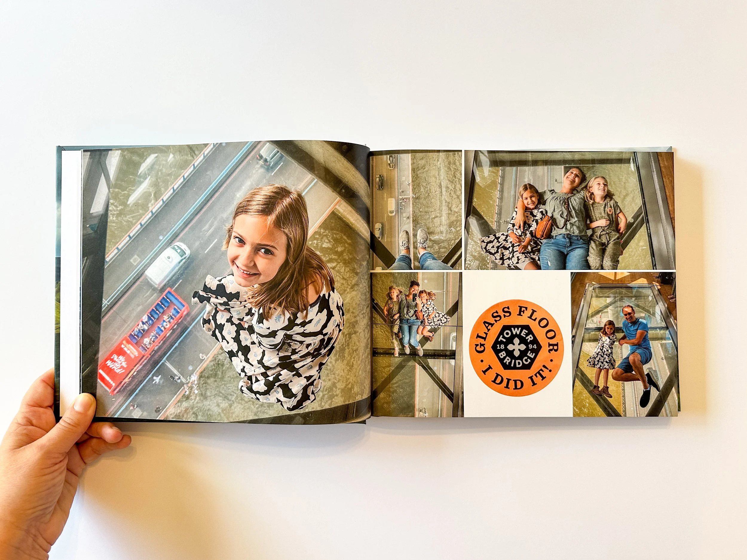 Open photo book showing photos of a family on a glass-floored observation deck of the Tower Bridge high above a city street below.  There is also a circular sign with an orange border and black text that reads 'Glass Floor I Did It!'