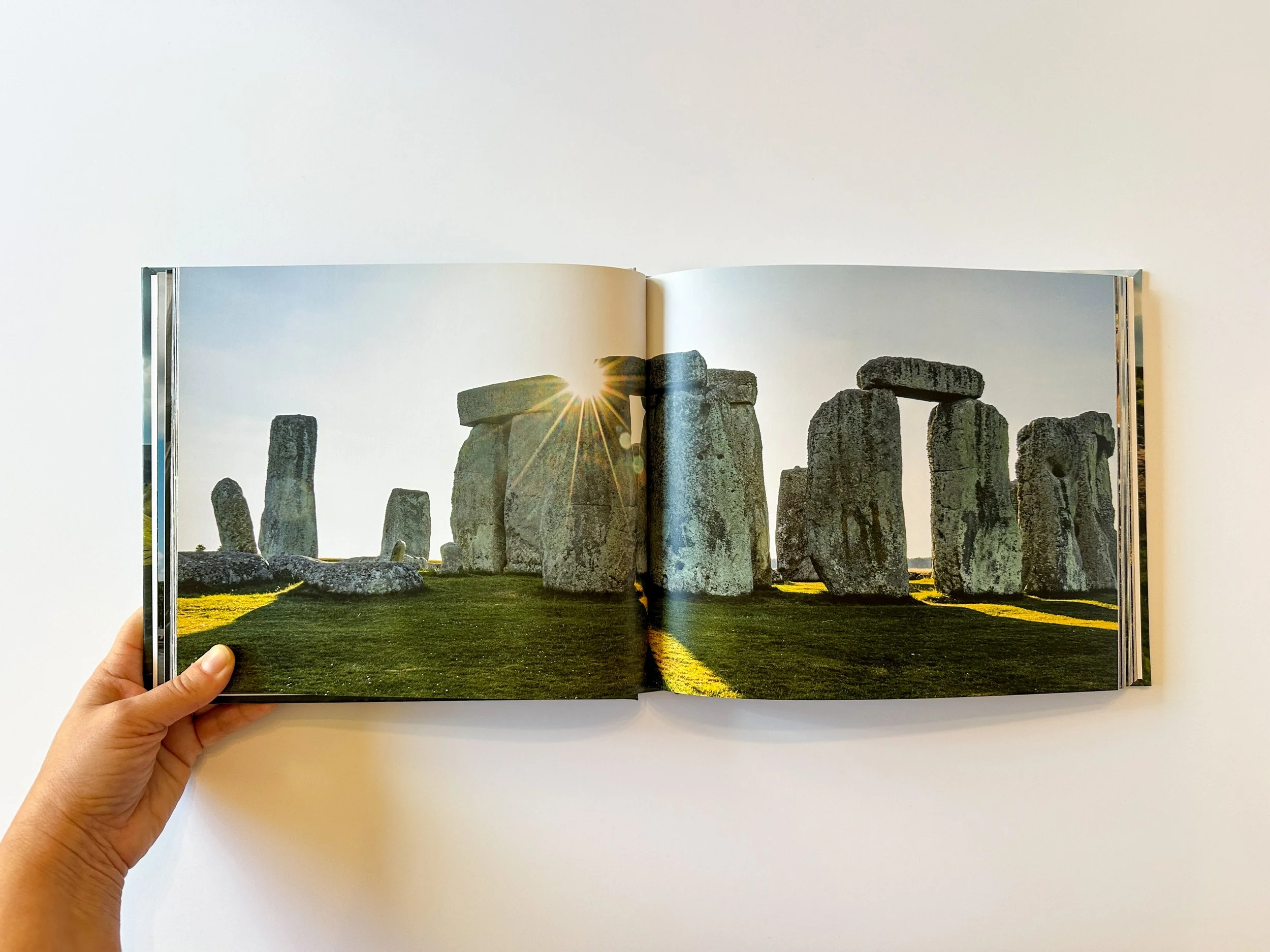 A photograph of Stonehenge, a prehistoric monument with large standing stones arranged in a circular layout, taken during sunset or sunrise with a sunburst peeking through the stones.