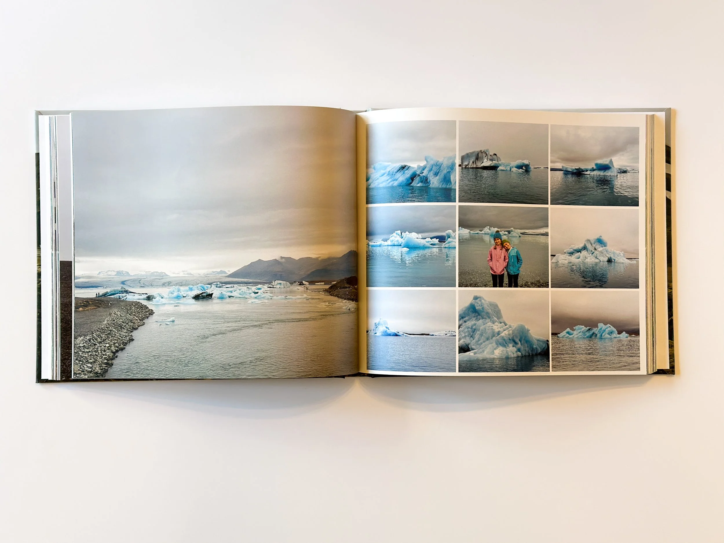Open photo book showing images of icebergs and a couple in jackets standing on a shoreline.