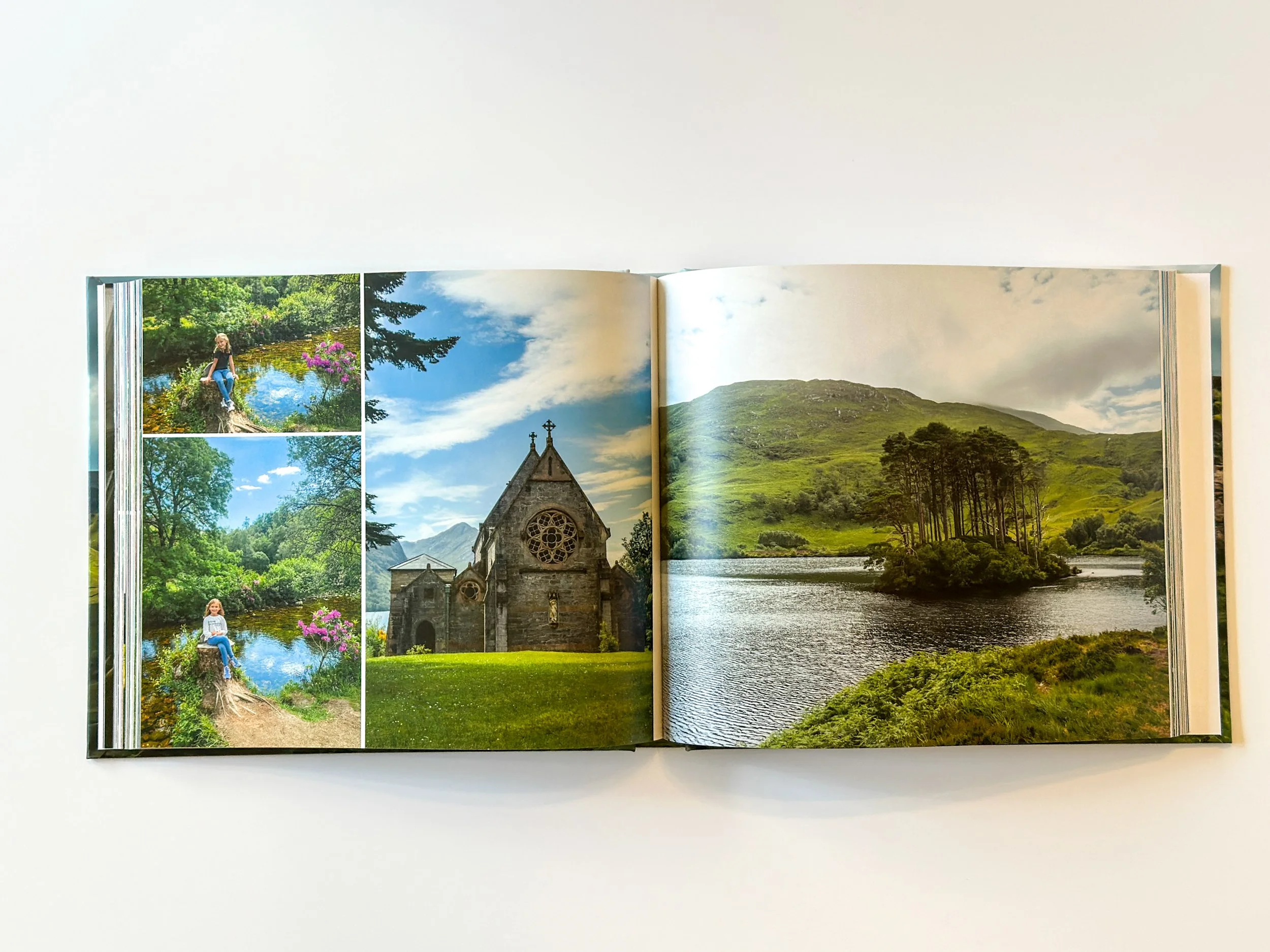 Open photo book showing images of a scenic lake, a church, and lush green hills with trees.
