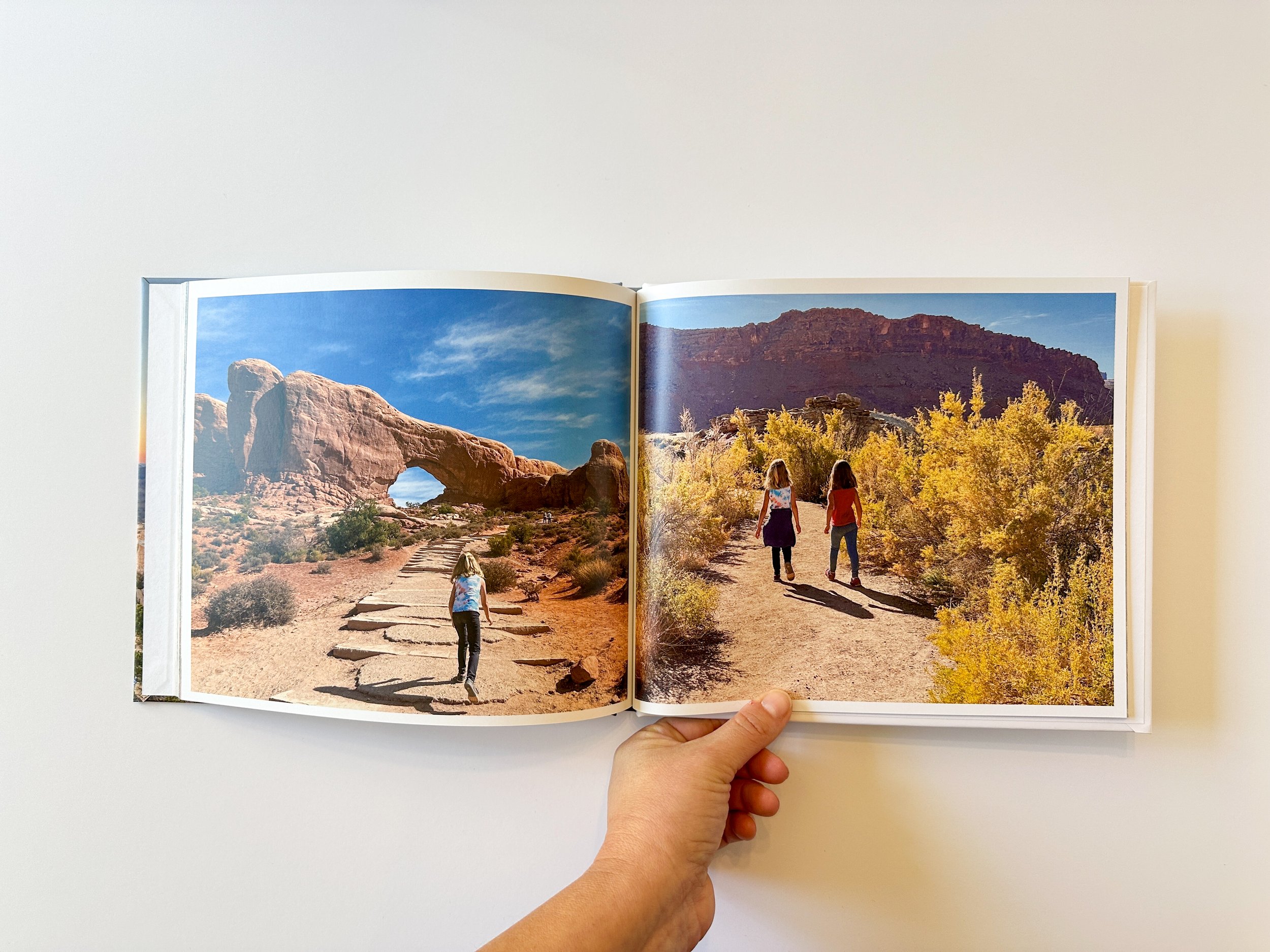 Open book showing two desert landscape in Arches National Park with three women walking on dirt paths surrounded by shrubs and rock formations.