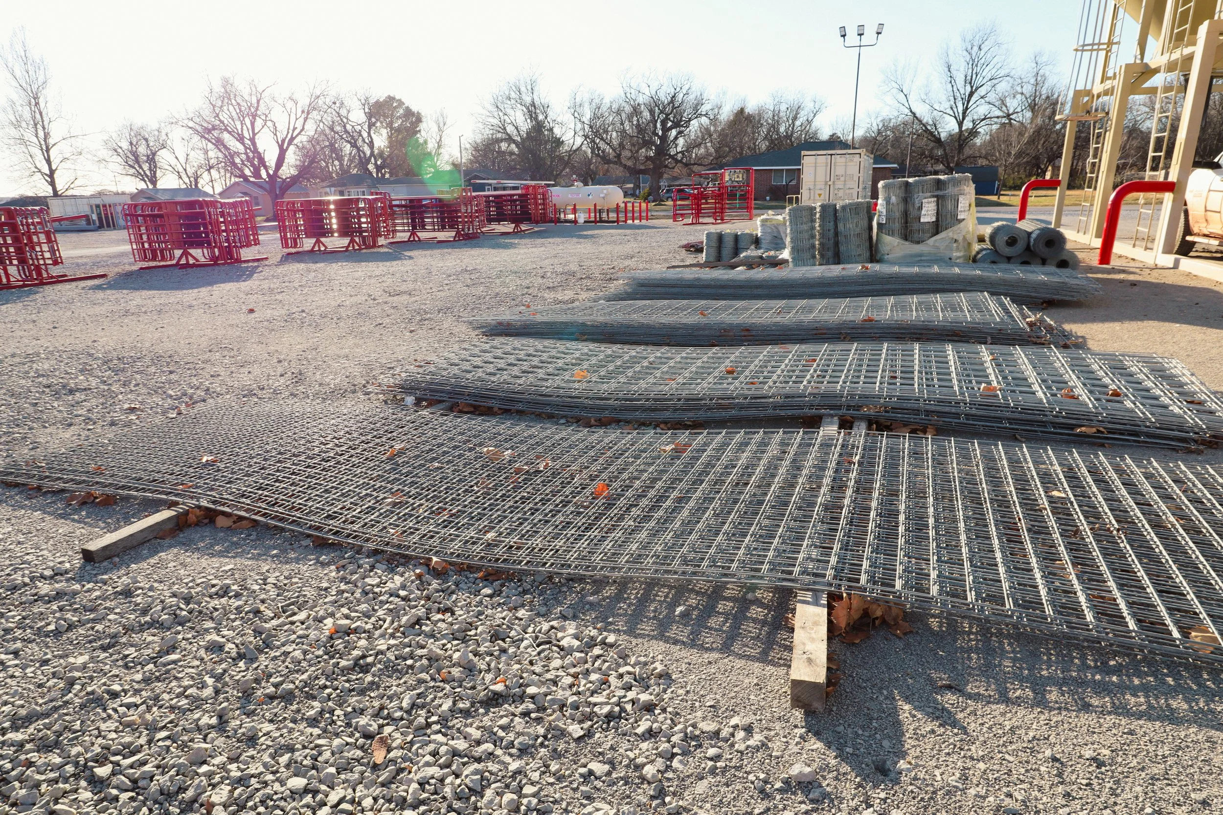 Livestock fence panel's laying in piles, gravel ground, and trees in the background.