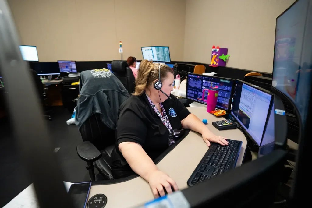Woman wearing a headset working at a desk with multiple computer monitors in an office environment.