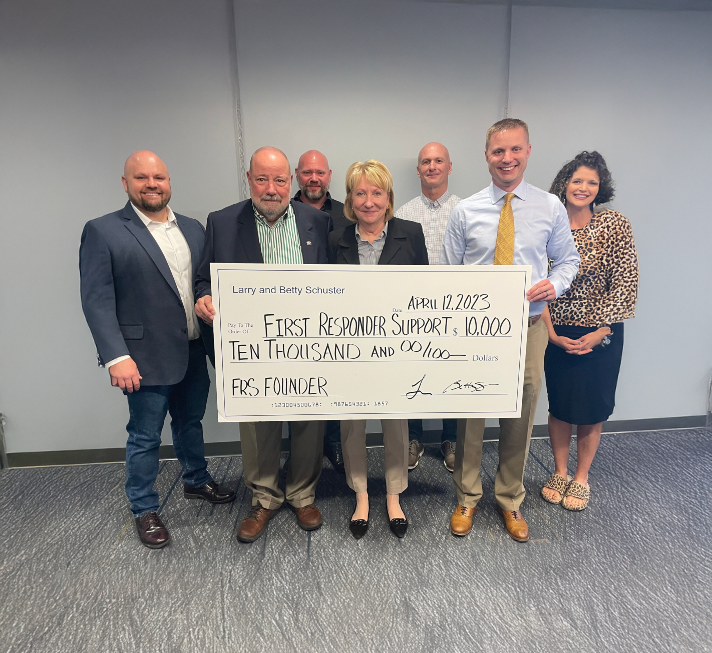Group of seven people standing indoors, holding a large check for $10,000, dated April 12, 2023, made out to First Responder Support.