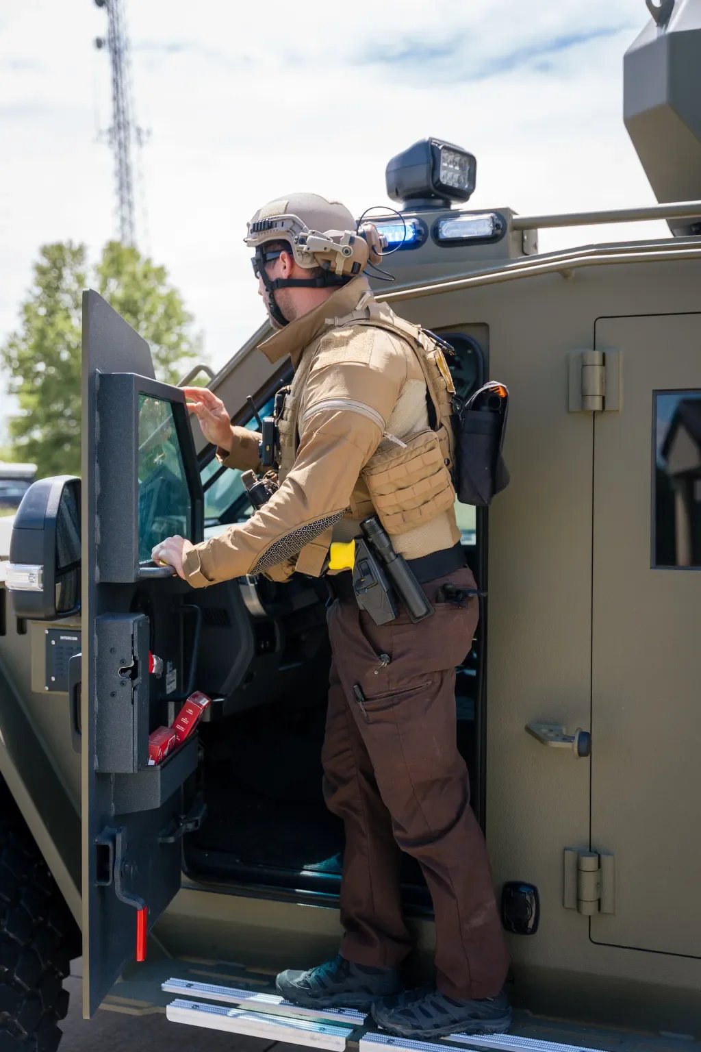 A military soldier in tactical gear standing beside a military vehicle, using a touchscreen monitor inside the vehicle.