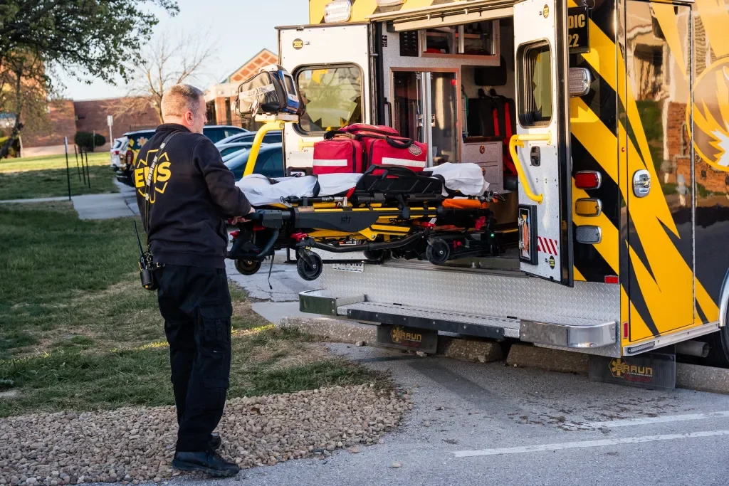 EMT nurse loading a stretcher into an ambulance parked outside.