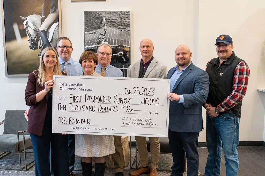 Group of seven people holding a large check made out to First Responder Support for $10,000, dated January 25, 2023, in a room with artwork on the wall, celebrating a donation.