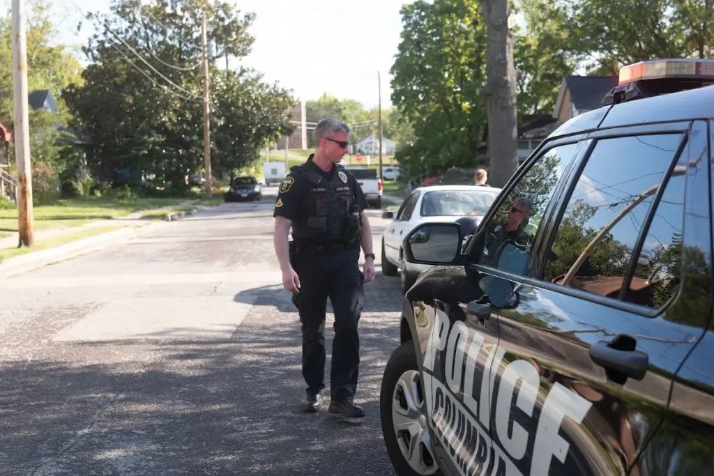 A police officer standing next to a police vehicle on a residential street.