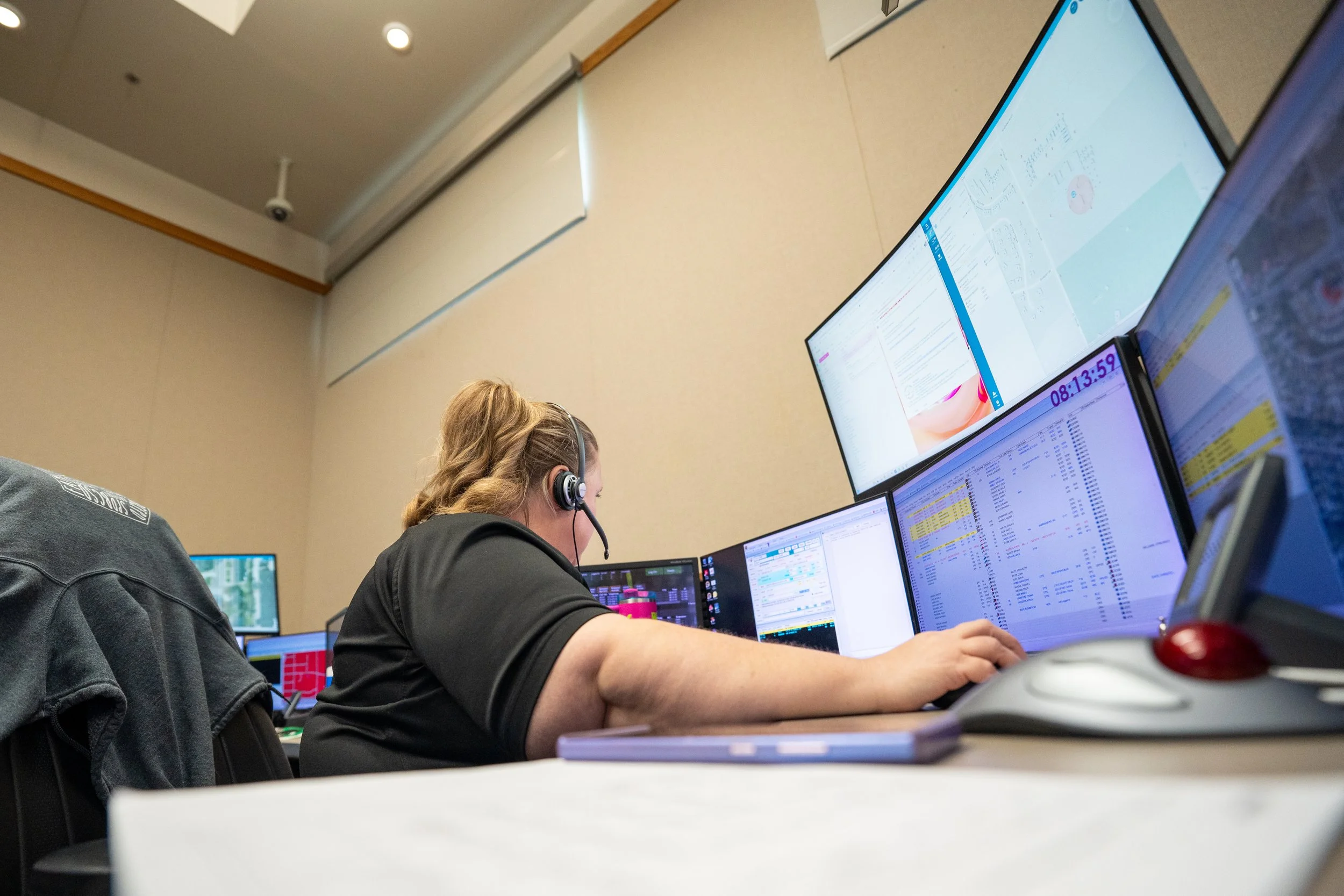 A woman wearing a headset using multiple computer monitors in an office setting.
