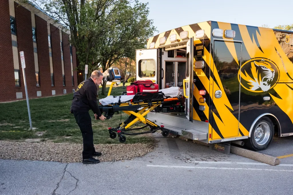 Emergency medical responder loading a stretcher into an ambulance with a tiger stripe design.