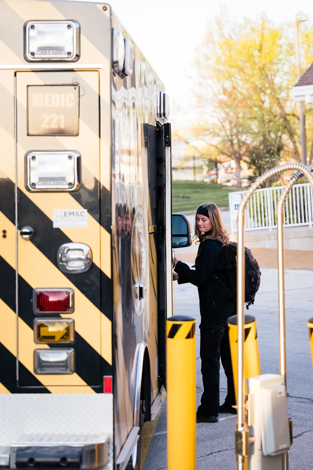 A woman with a backpack gets into a yellow and black emergency medical services ambulance.