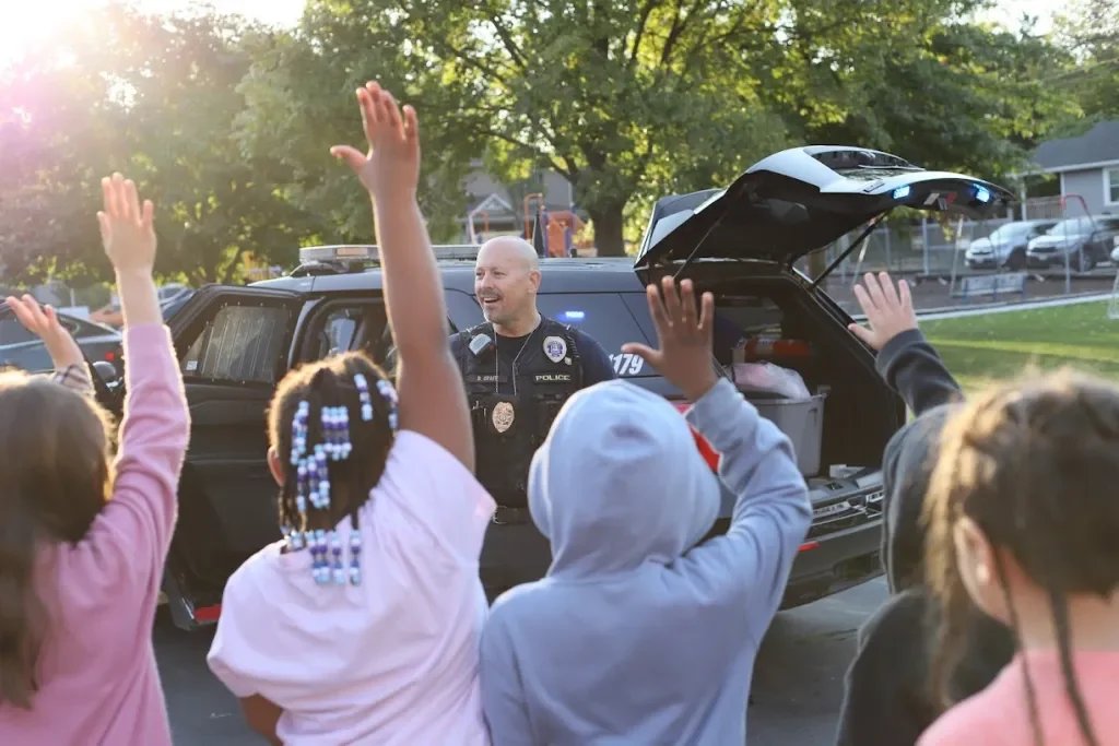 Police officer talking to children raising their hands in a park or playground.