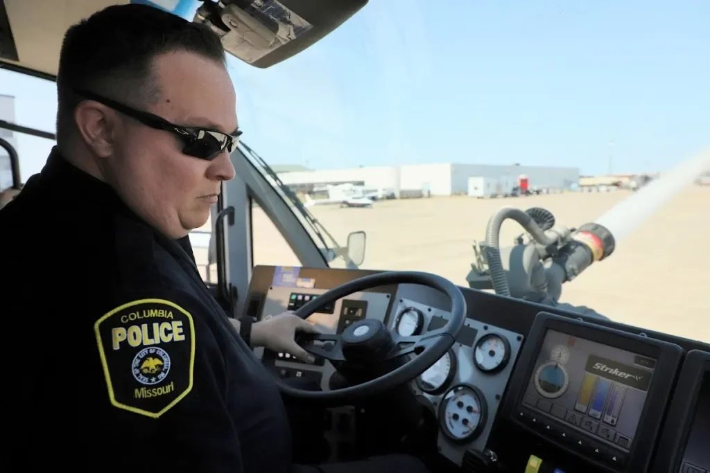 A police officer wearing sunglasses and a Columbia Police Missouri uniform sitting in the cockpit of a helicopter.