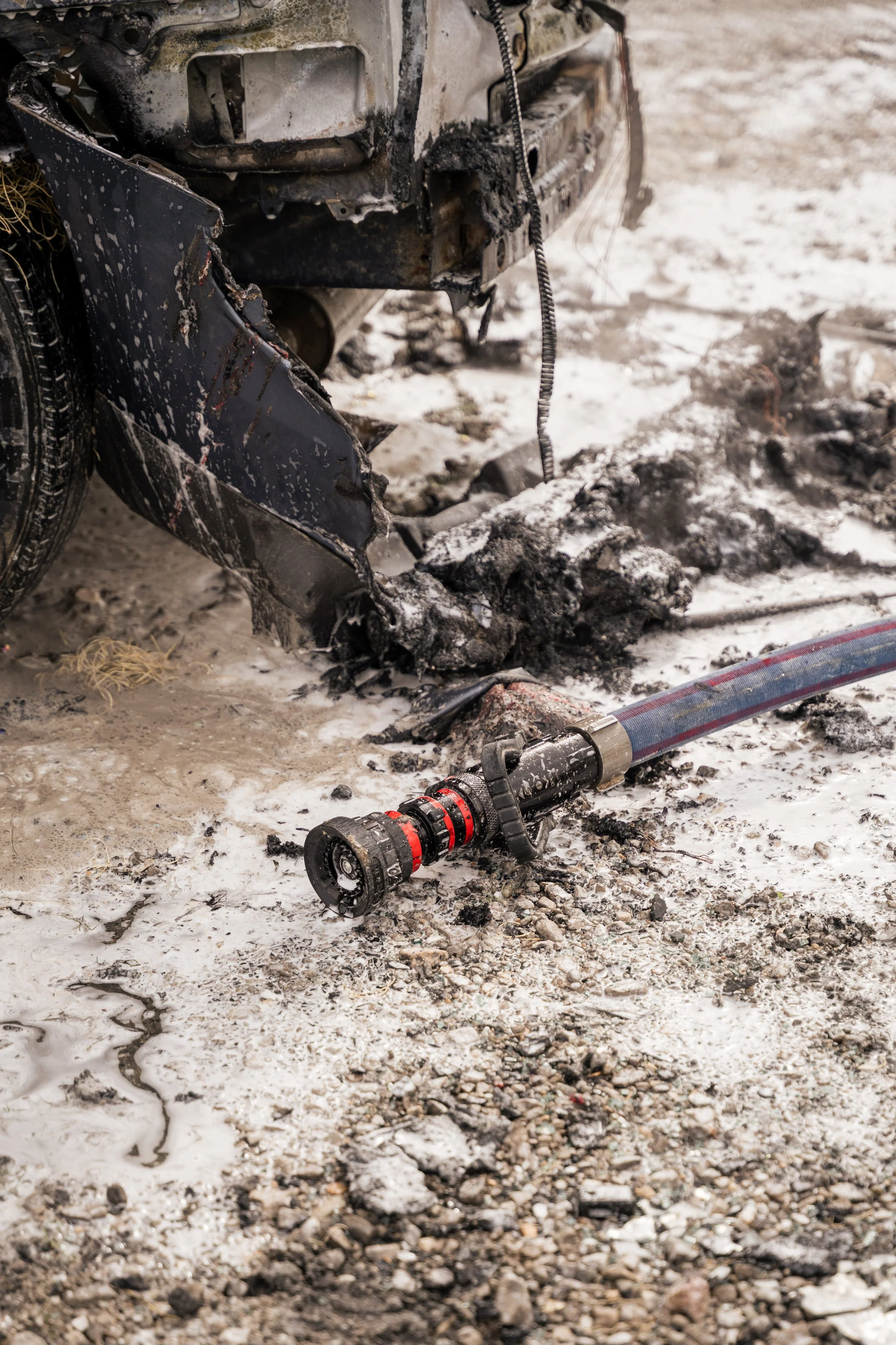 Burned and damaged vehicle with fire hose on snowy ground.