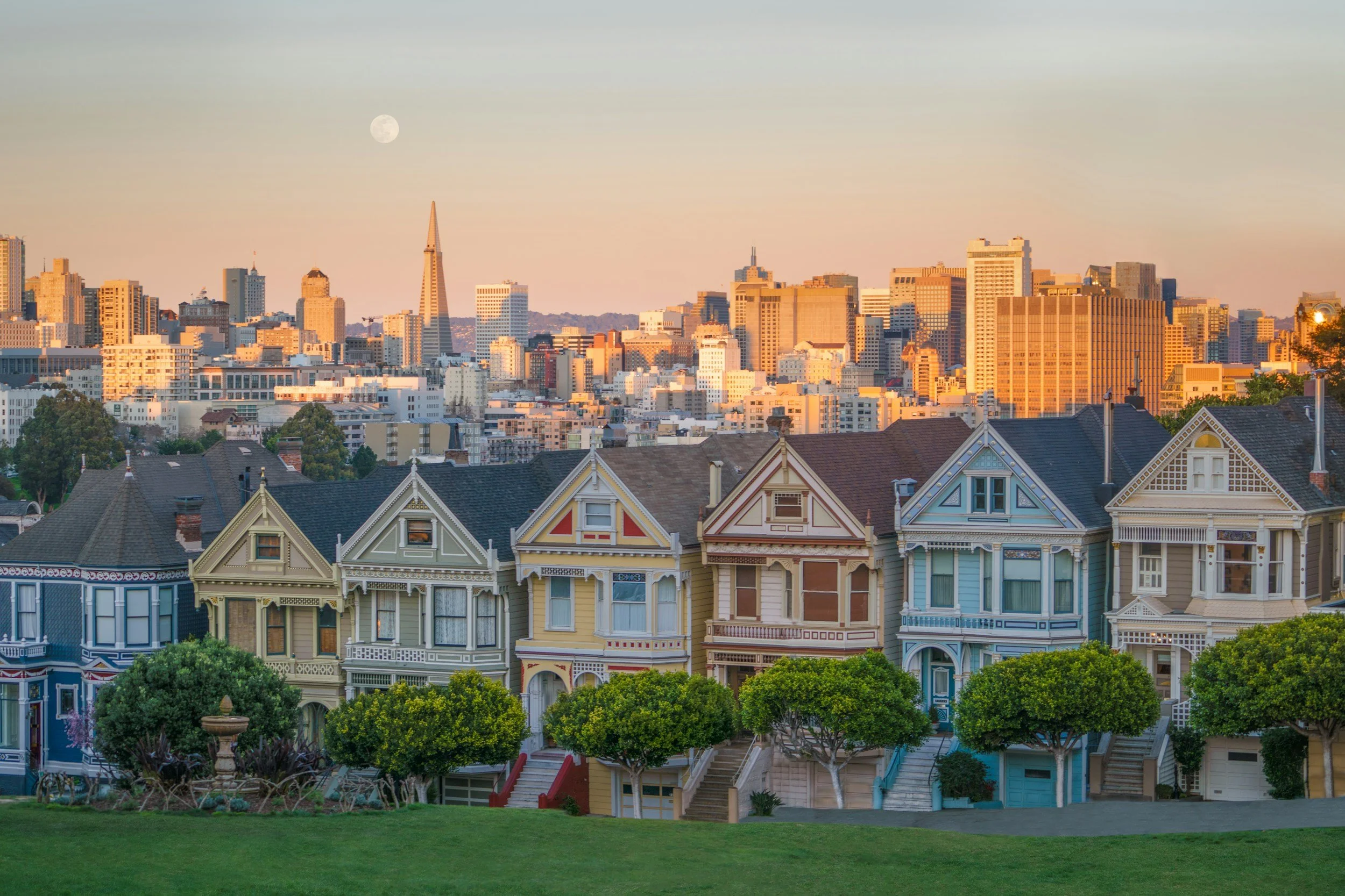 Colorful historic Victorian houses, known as the Painted Ladies, with the modern San Francisco skyline in the background during sunset.
