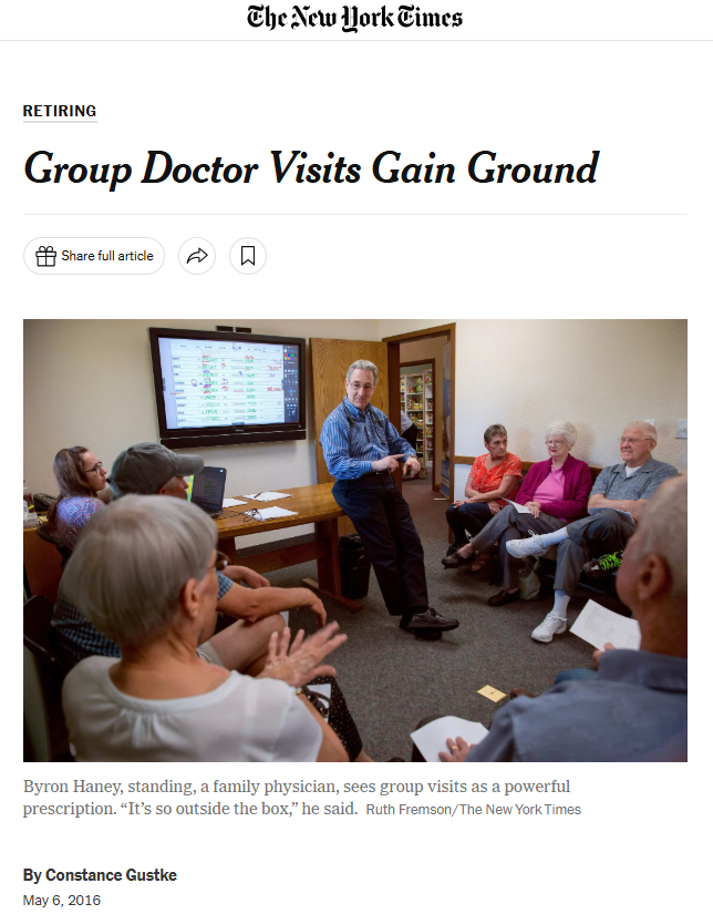 A group of elderly people seated in a small room, listening to a man standing near a television screen, which displays a colorful chart or presentation. The man appears to be explaining something to the group.