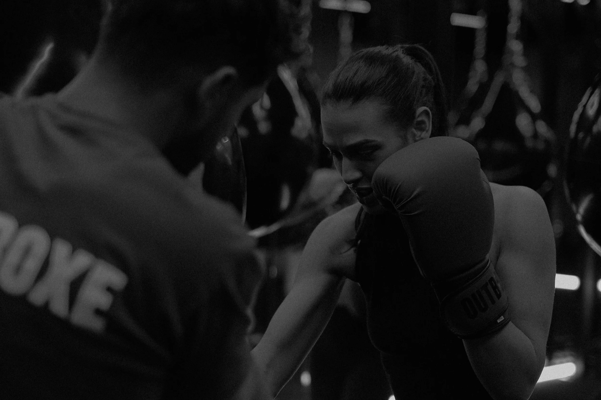 Une femme boxeuse s'entraînant avec un entraîneur dans une salle de gym sombre.