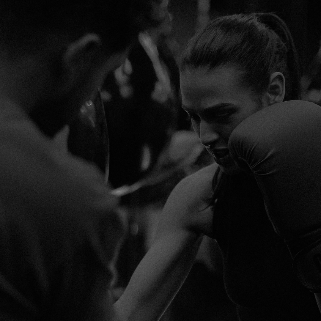 Une femme reçoit un coup de poing au visage lors d'un entraînement de boxe, dans une ambiance sombre.