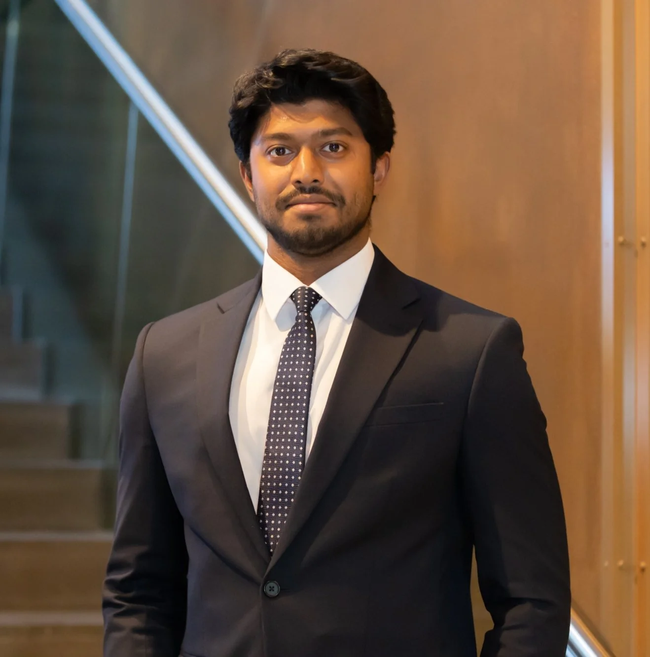 A man with dark hair, beard, and mustache standing with arms crossed in a rocky cave with warm lighting.