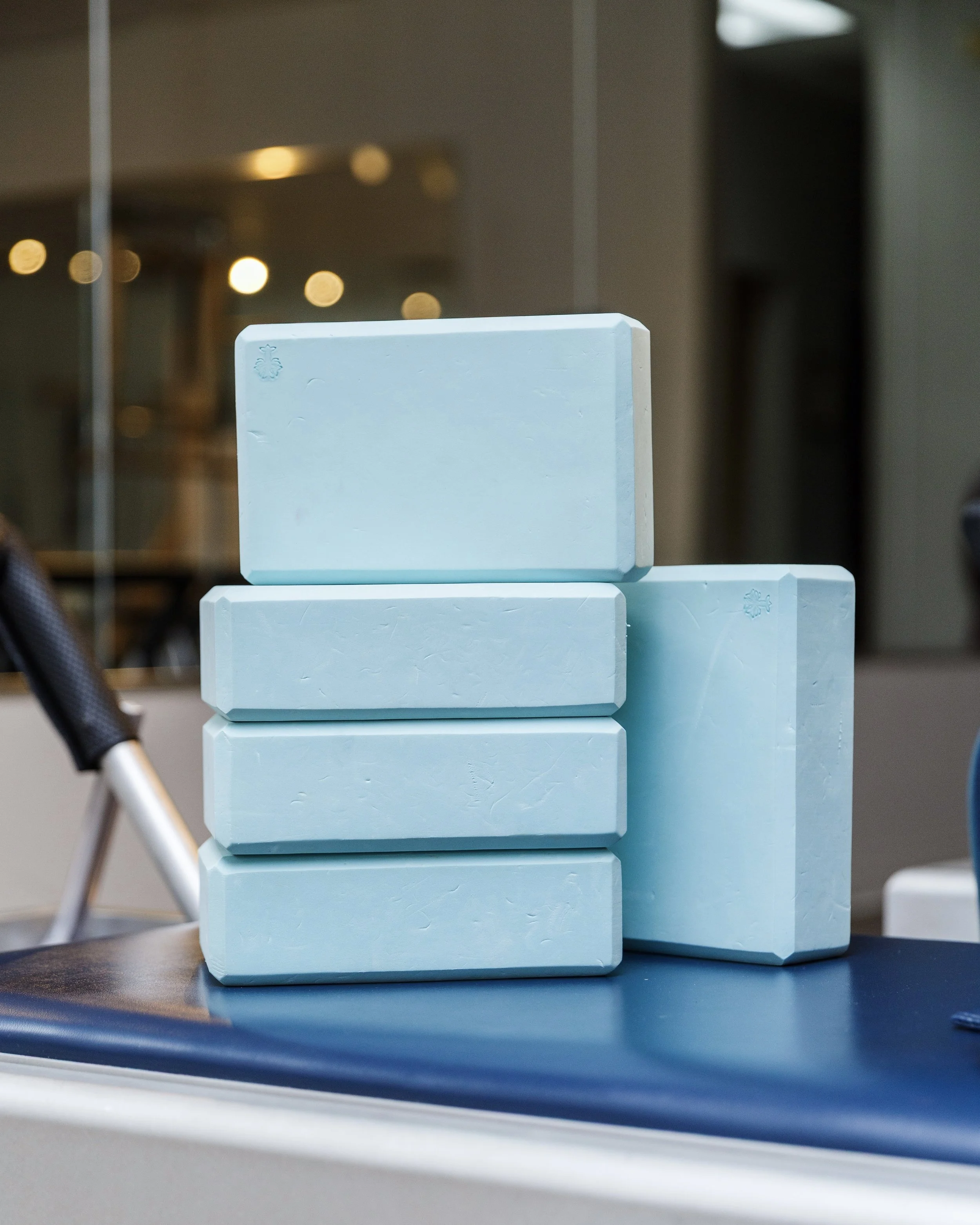Stacked light blue foam yoga blocks used in studio at providence pilates on a dark blue yoga mat.
